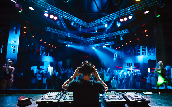Disc jockey mixing electronic music in club people are dancing