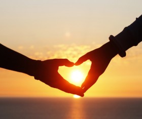 Heart shape of hands against sea during sunset Stock Photo