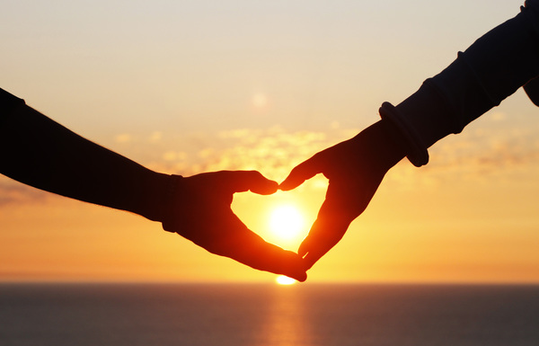 Heart shape of hands against sea during sunset Stock Photo