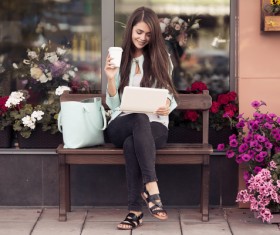 Sitting on a bench in front of a flower shop to play a girl on the computer coffee
