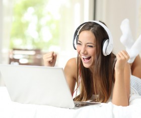 Smiling girl with white headphones and laptop lying in bed Stock Photo