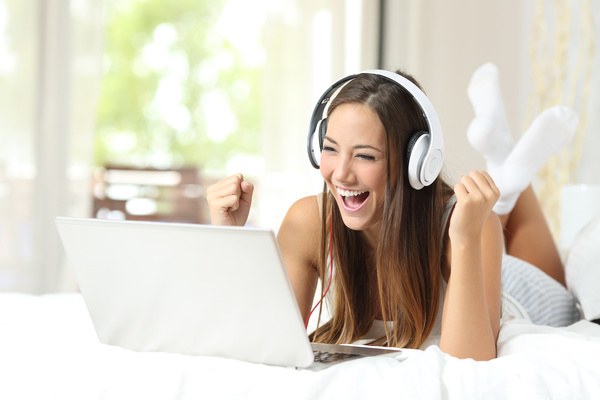 Smiling girl with white headphones and laptop lying in bed Stock Photo