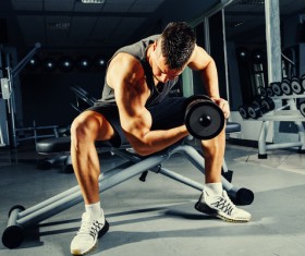 Strong muscular bodybuilder doing exercise with dumbbell in the gym