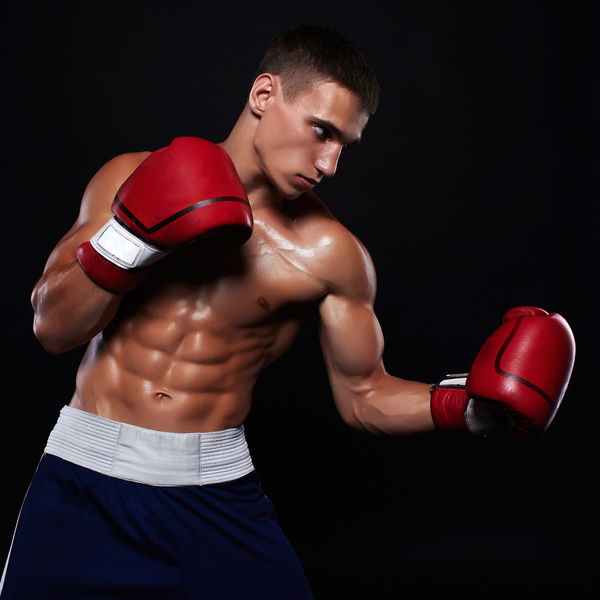 The young male athlete kickboxing on a black background