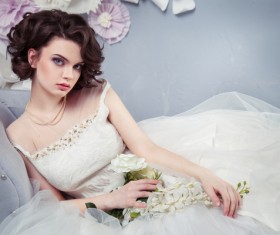 Woman wearing a wedding dress holding flowers sitting on the couch