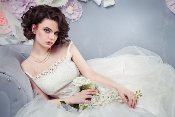 Woman wearing a wedding dress holding flowers sitting on the couch