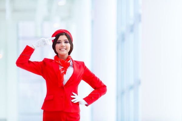 Young beautiful flight attendant with tribute to white background Stock Photo