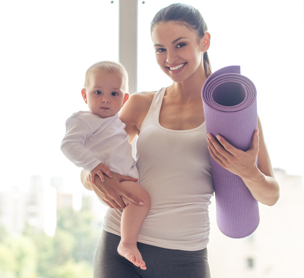 Young mother holding the baby holding a yoga mat Stock Photo