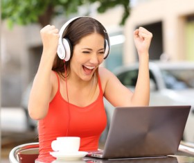 Young woman with headset holding hands cheering with laptop