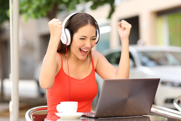 Young woman with headset holding hands cheering with laptop