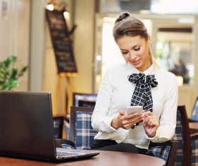 Young woman looking at mobile phone with information on laptop