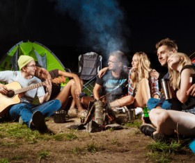 Camping friends sitting around the campfire to play guitar Stock Photo