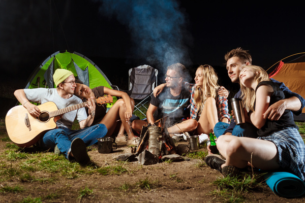 Camping friends sitting around the campfire to play guitar Stock Photo