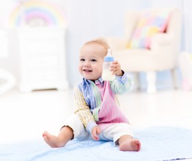The baby sitting on the floor holding the bottle Stock Photo