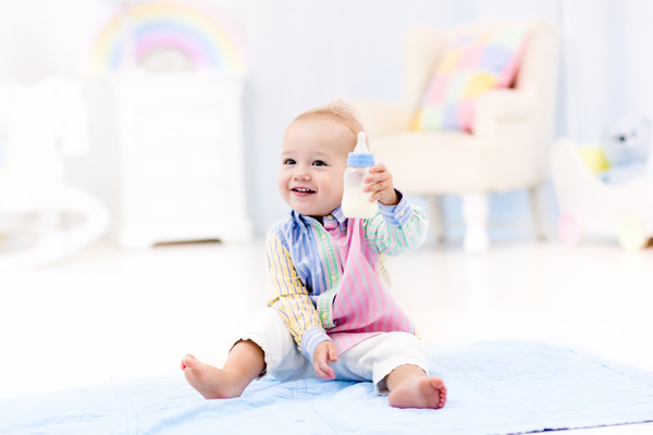 The baby sitting on the floor holding the bottle Stock Photo