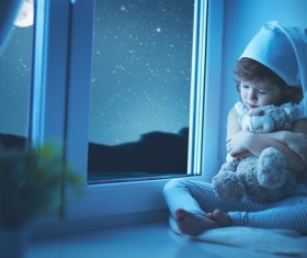 little girl sitting on the windowsill with a teddy bear Stock Photo