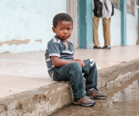 black tiny boy sitting on walkway Stock Photo