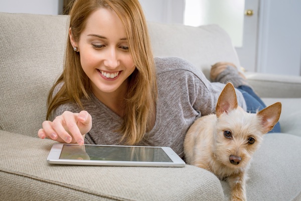 A girl and a pet dog lying on a sofa playing with a tablet computer Stock Photo