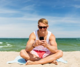 The man sitting on the beach plays the smartphone Stock Photo