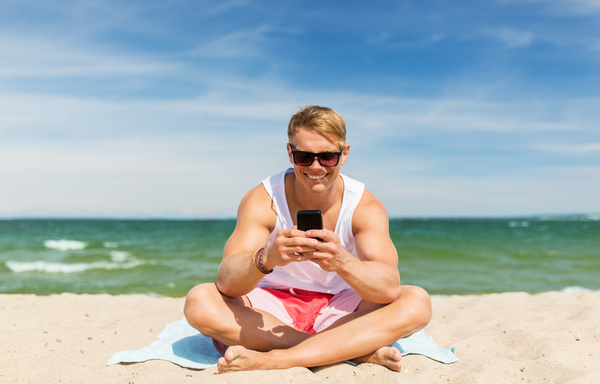 The man sitting on the beach plays the smartphone Stock Photo