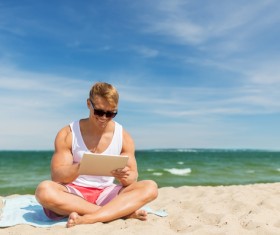 The man sitting on the beach plays the tablet Stock Photo