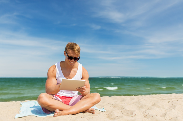 The man sitting on the beach plays the tablet Stock Photo