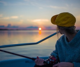 Young woman fishing on lake at sunset Stock Photo