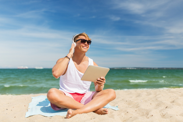 man sitting on the beach listening to music with a Tablet PC Stock Photo