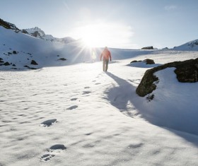 Human walking on snowy mountain land under sunlight Stock Photo