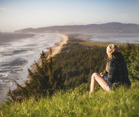 Woman sitting on the hillside watching the sea Stock Photo
