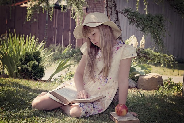 little girl sitting on the grass reading Book Stock Photo