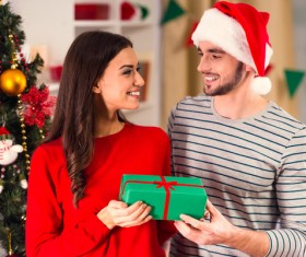 Couple Beside Christmas Tree Holding Gift Stock Photo