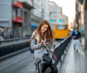 Girl sitting on the parapet playing phone Stock Photo
