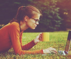 Girl lying on the grass drinking coffee using laptop Stock Photo