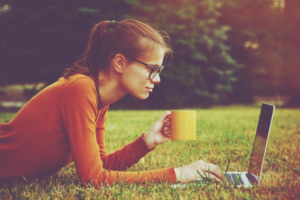 Girl lying on the grass drinking coffee using laptop Stock Photo