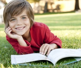 Little boy reading book lying on the grass Stock Photo