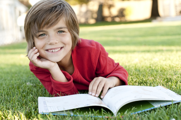 Little boy reading book lying on the grass Stock Photo