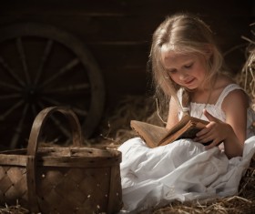 Little girl reading book sitting on haystack Stock Photo