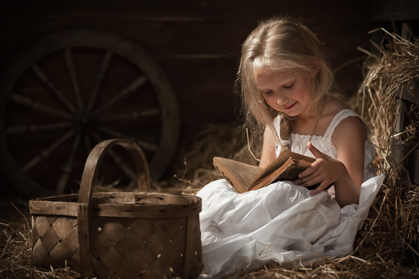 Little girl reading book sitting on haystack Stock Photo