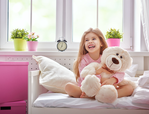 Little girl sitting in bed hugging teddy bear Stock Photo