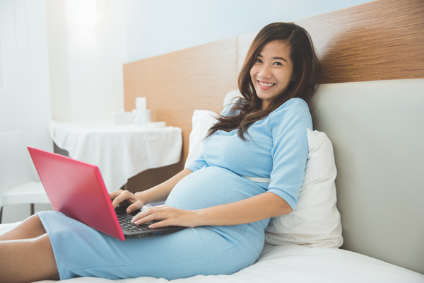 Pregnant woman in bed using laptop Stock Photo