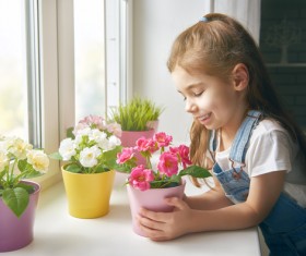 little girl looks at the flowers on the windowsill Stock Photo