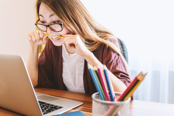 Girl biting pencil working in front of laptop Stock Photo