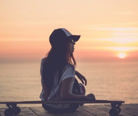 girl leaning on the skateboard watches sunrise Stock Photo
