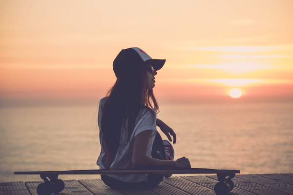 girl leaning on the skateboard watches sunrise Stock Photo