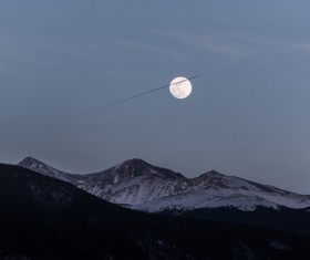 Bright moon above snowy mountain range Stock Photo