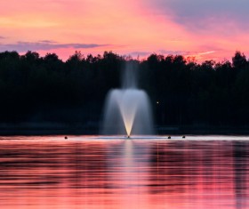 Water fountain on calm lake at dusk Stock Photo