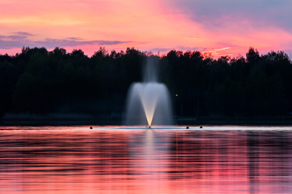 Water fountain on calm lake at dusk Stock Photo