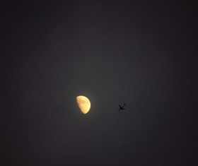 Flying plane and bright crescent on dark sky Stock Photo