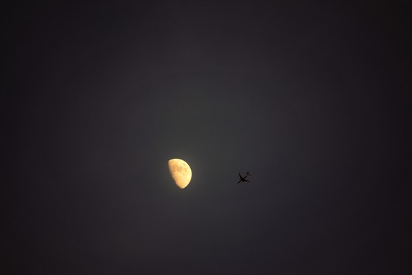Flying plane and bright crescent on dark sky Stock Photo